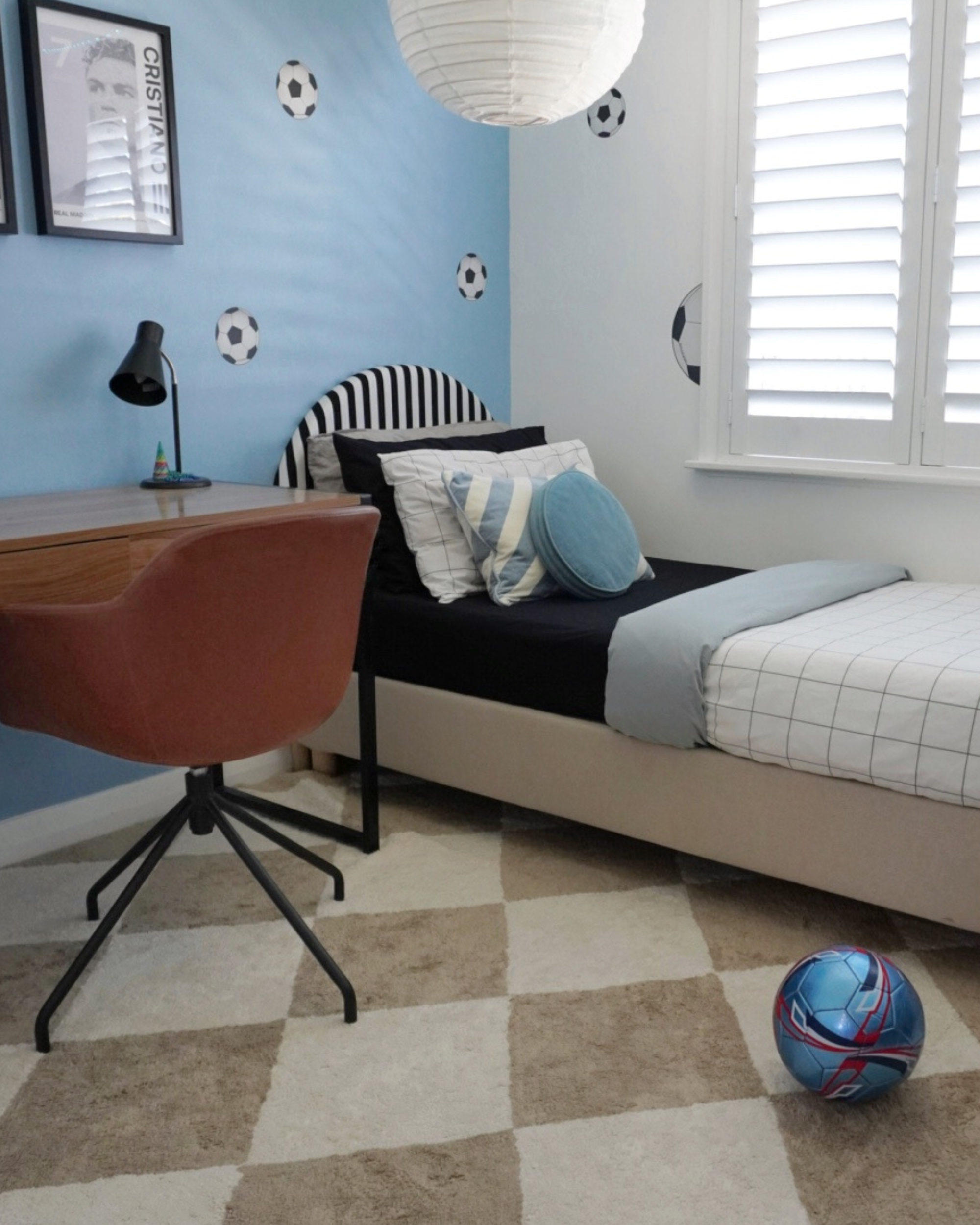 Children's bedroom with blue walls, bed, desk, and sports-themed decor.