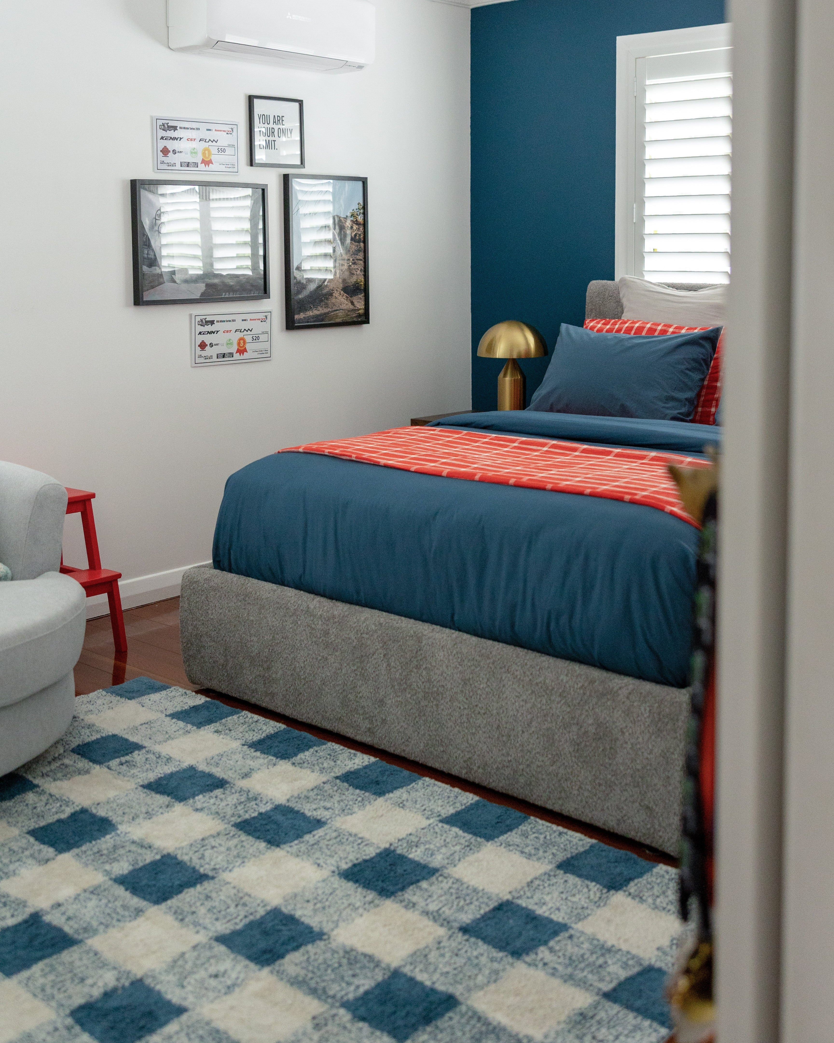 Bedroom with blue walls, checkered rug, and framed pictures on the wall.