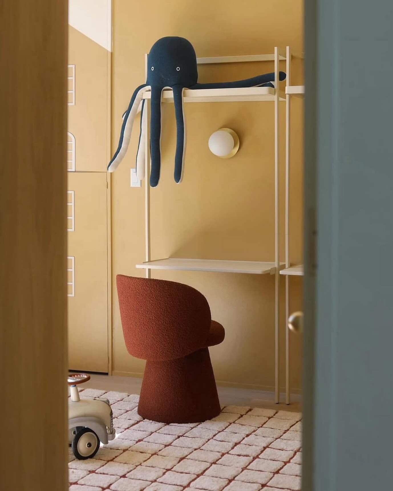 Children's room with a red chair, yellow walls, and a blue octopus toy on a shelf.