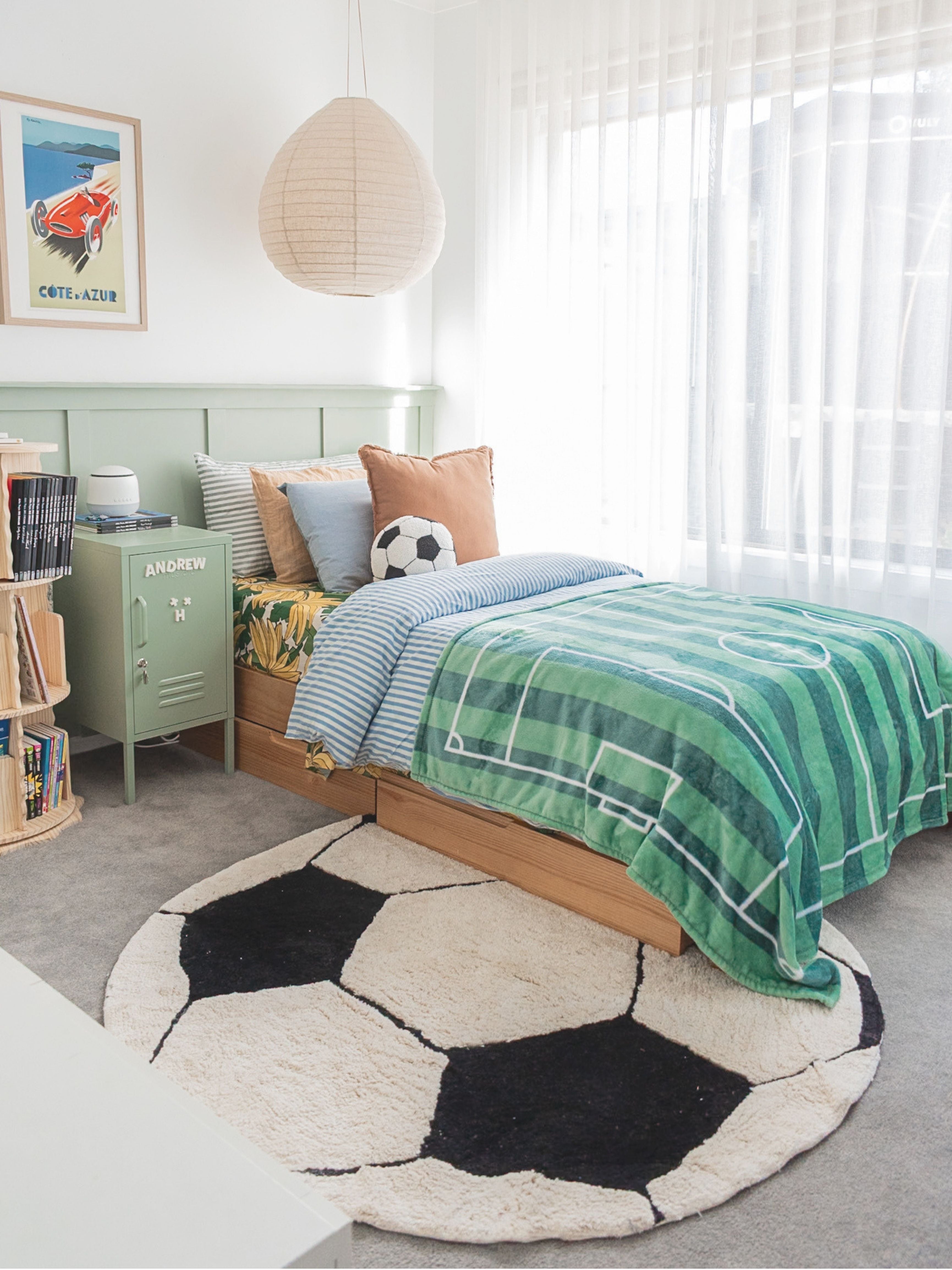 Children's bedroom with a green plaid blanket on a bed, soccer ball rug, and colorful bedding.
